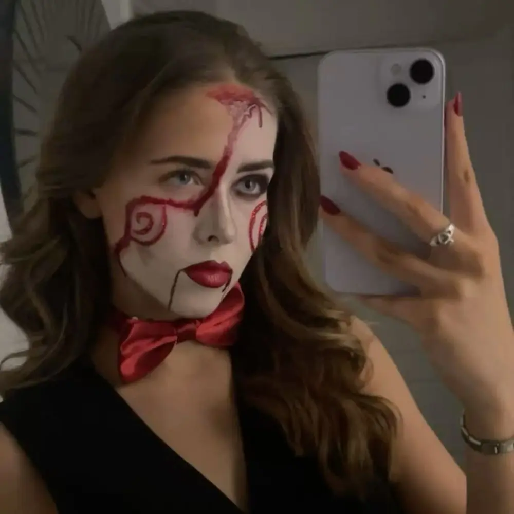 Glam Jigsaw makeup with pale skin, fine red spiral details, softly sculpted cheeks, blush, highlighter, and red lip