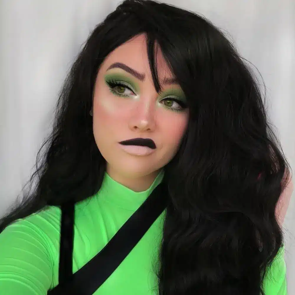 Shego makeup with green toned skin, a sharp black wing, smoky outer corners, dark lips, and bright cheek highlights