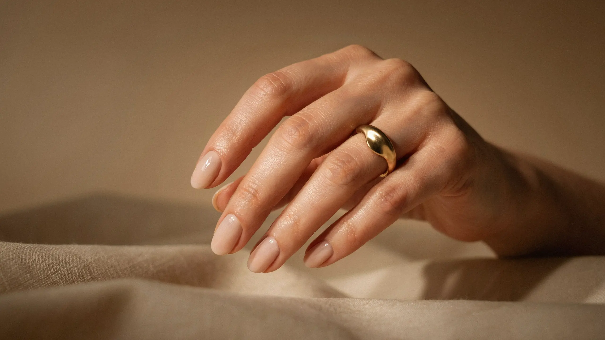 Hand with skin matching beige nude nails resting softly on fabric with a subtle clean manicure appearance