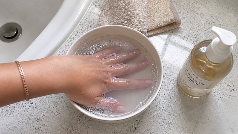 Hand soaking method showing warm soapy water treatment for removing fresh and dried nail glue residue