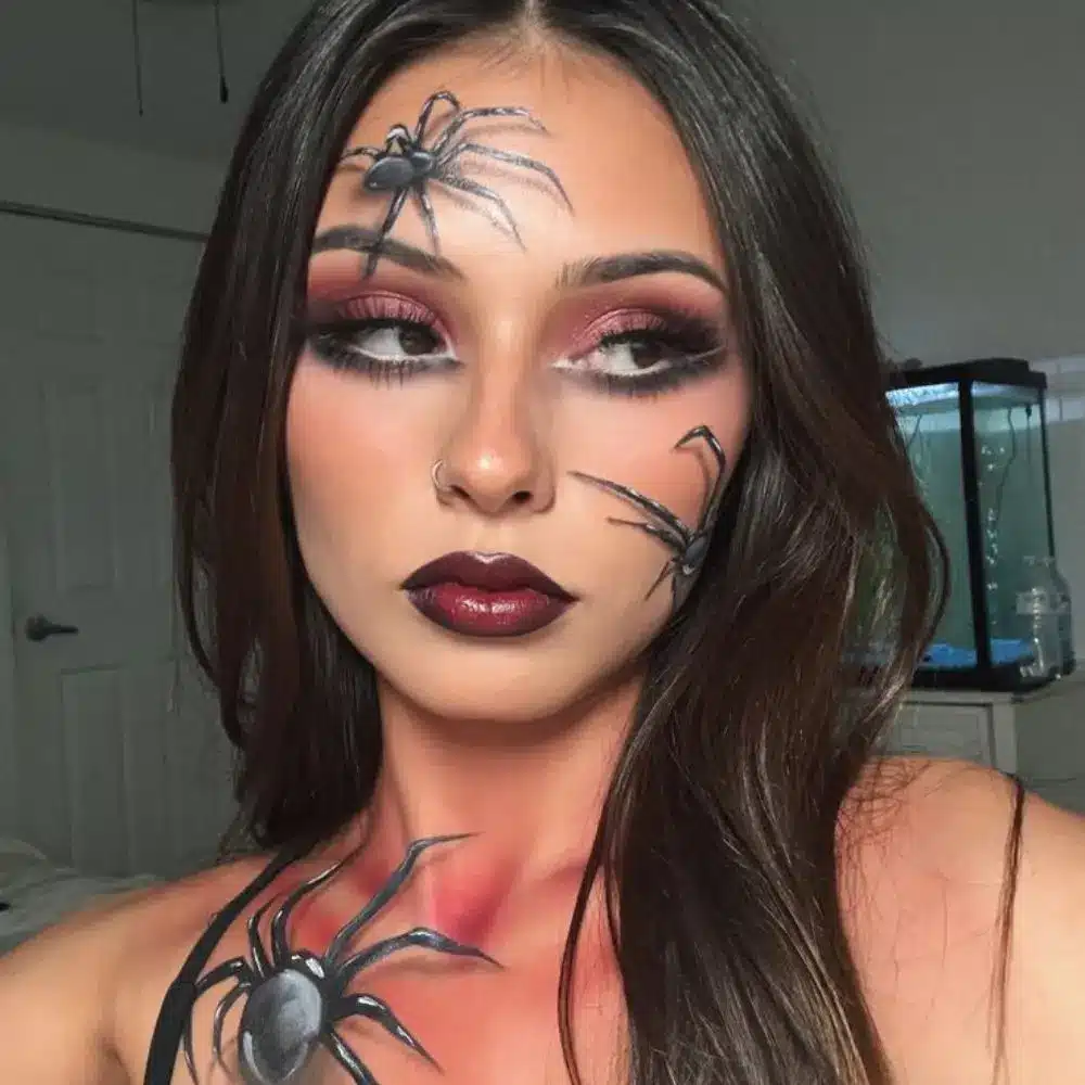 Spider glam makeup with a black web around one eye, a small spider detail, smoky shadow, full lashes, and dark lips