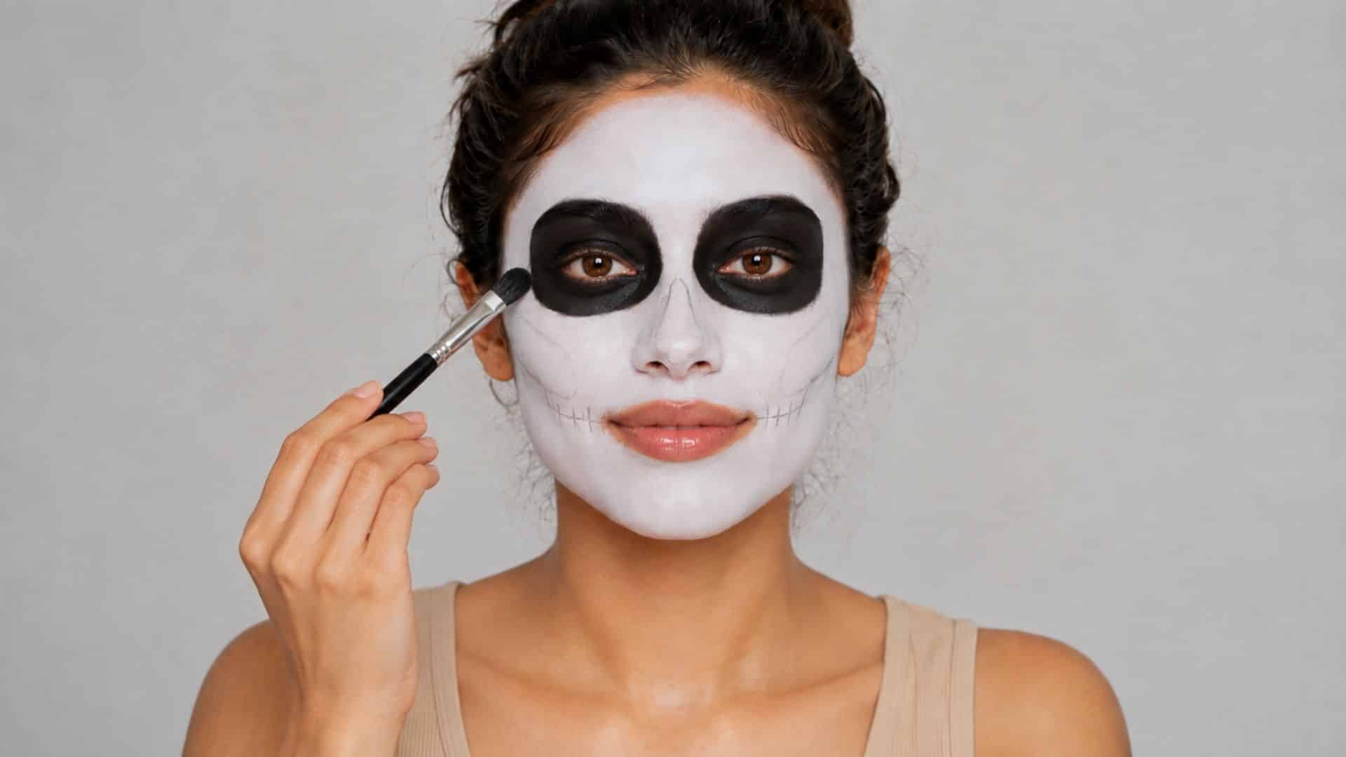 Woman applying black makeup around her eyes to create skeleton eye sockets.