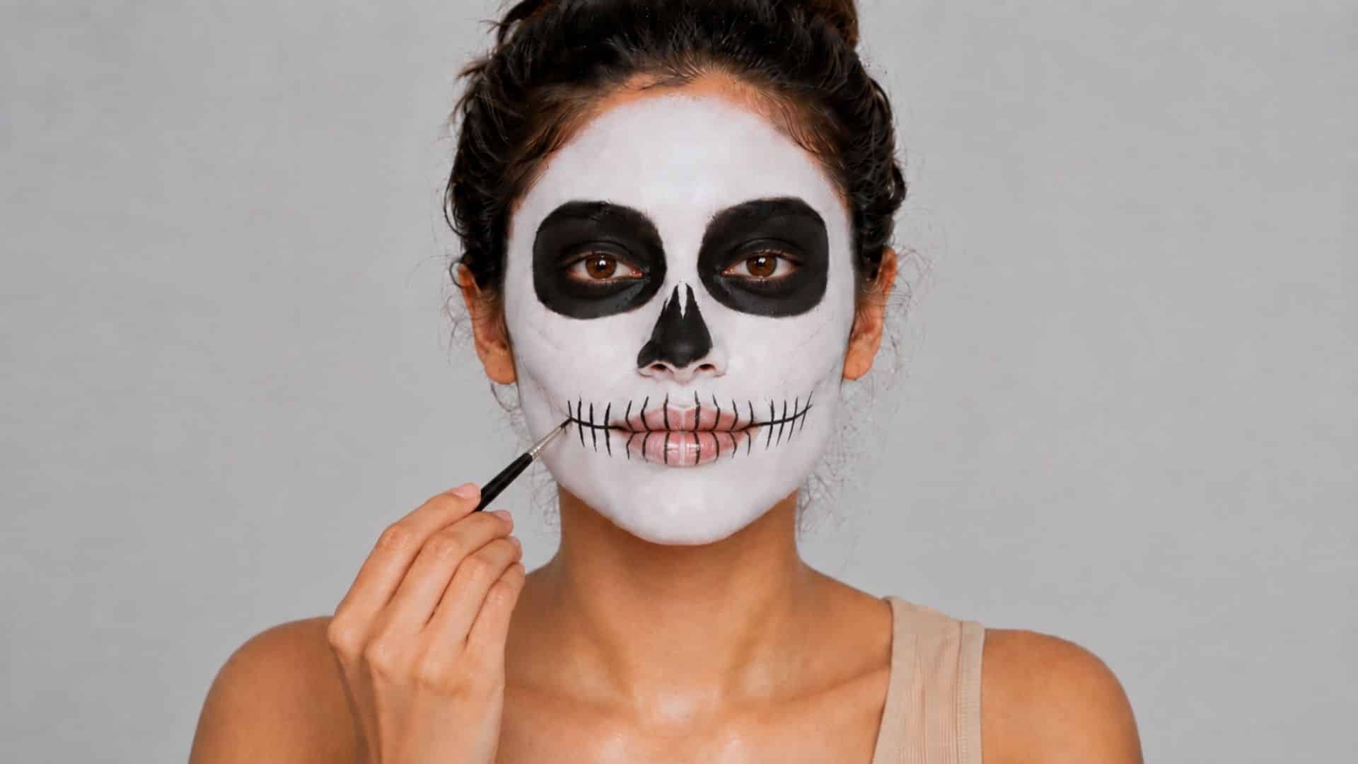 Woman drawing skeletal teeth lines across her mouth with black makeup.
