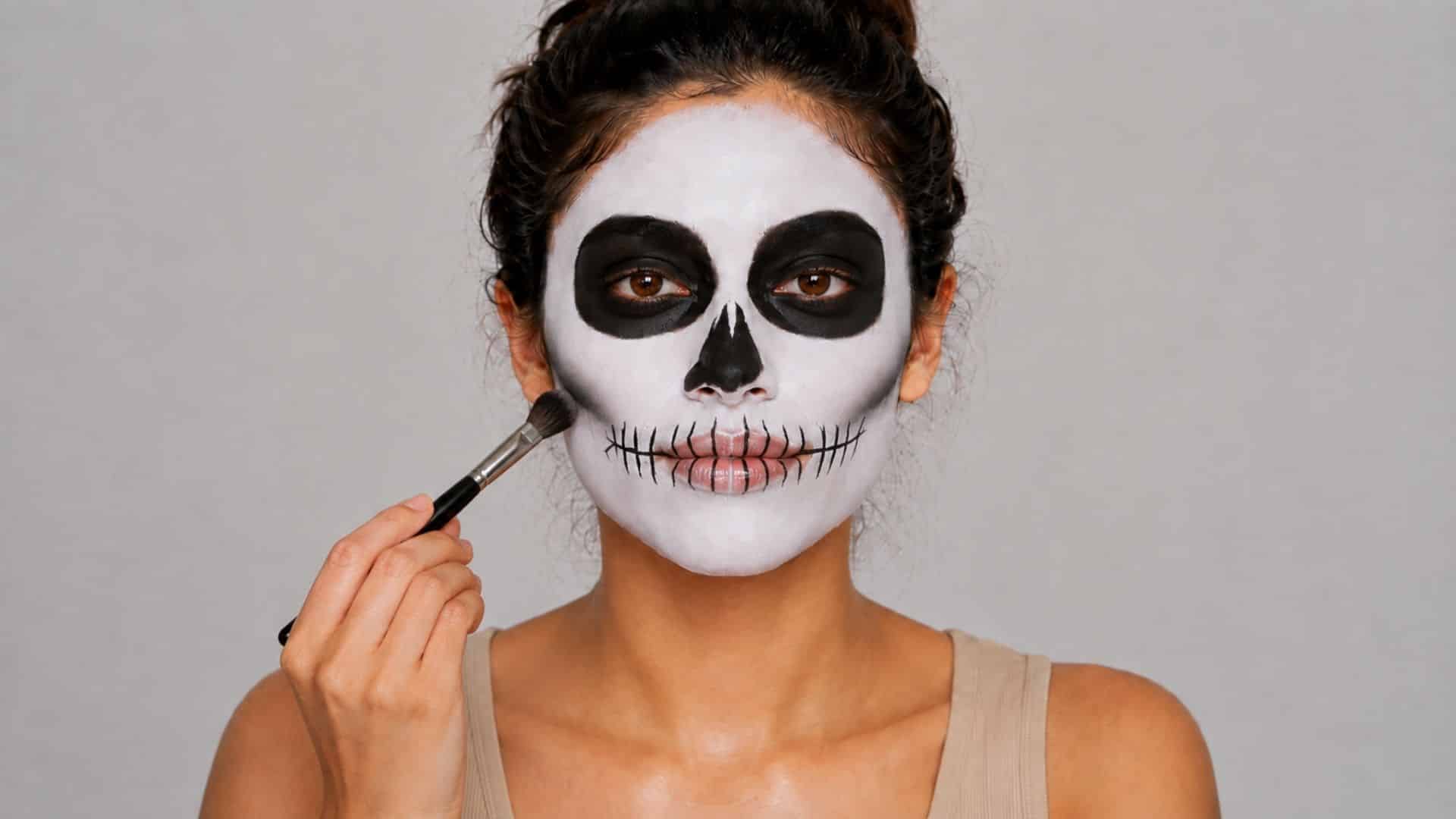Woman adding black and gray shading beneath her cheekbones for skeleton makeup.