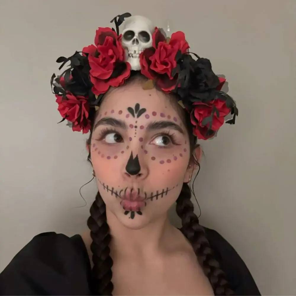 Sugar skull makeup with a white base, dark eye sockets and nose, stitched red lips, and vibrant symmetrical florals