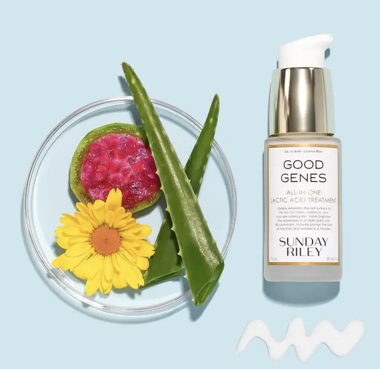 Skincare bottle next to aloe vera, yellow flower, and dragon fruit on blue background