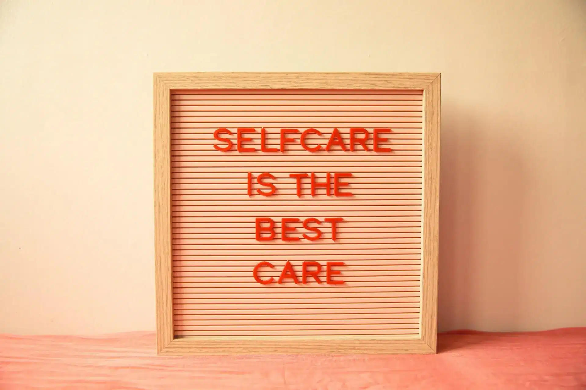 Wooden framed letter board with red text on pink background in softly lit room