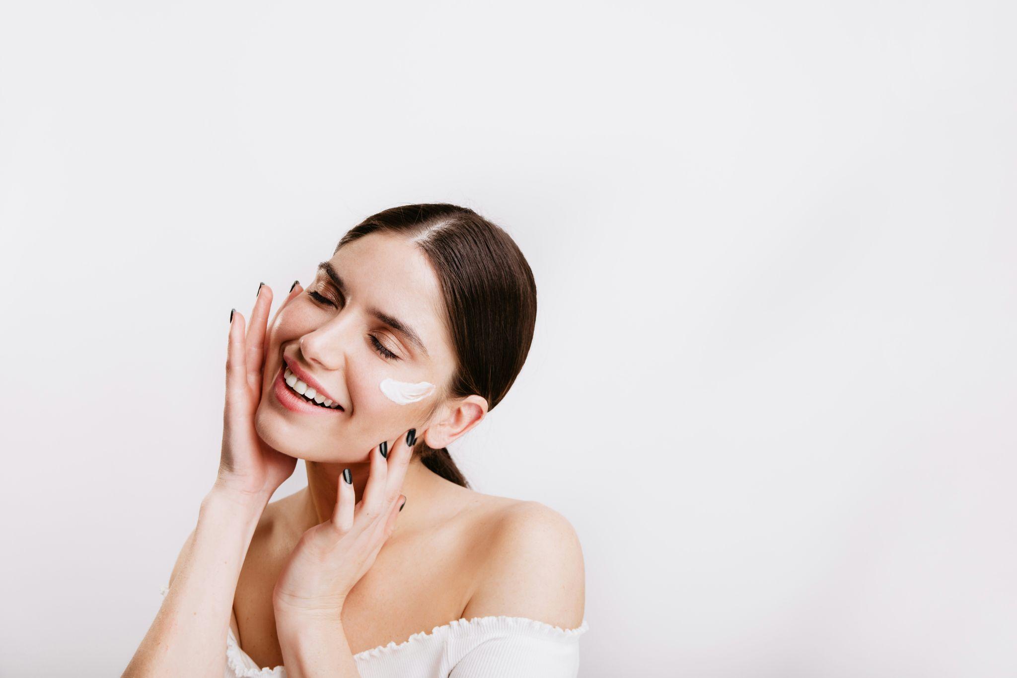 Smiling woman applying cream to face in bright minimalist setting