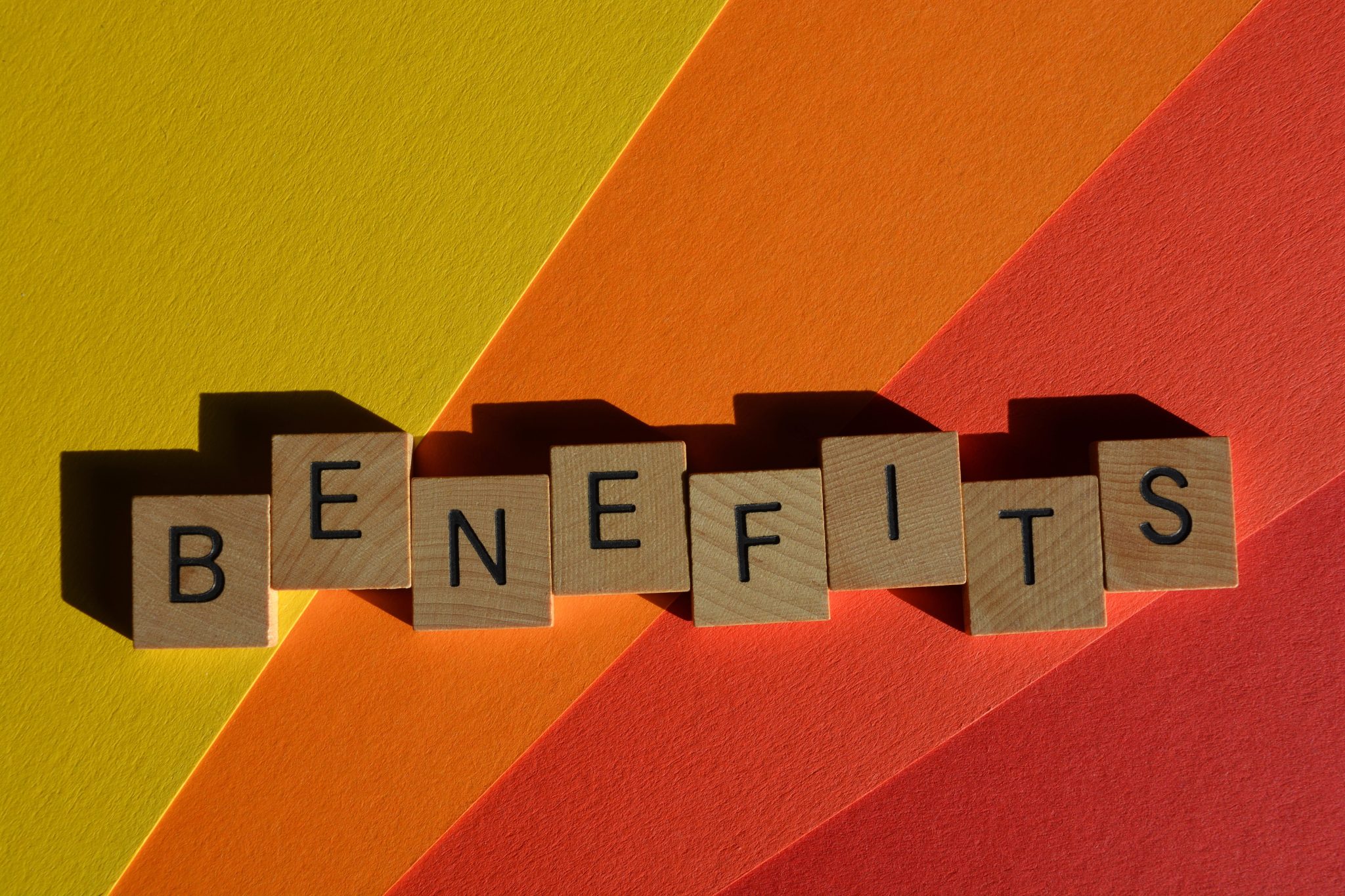 Wooden letter tiles spelling "benefits" on colorful yellow and orange background