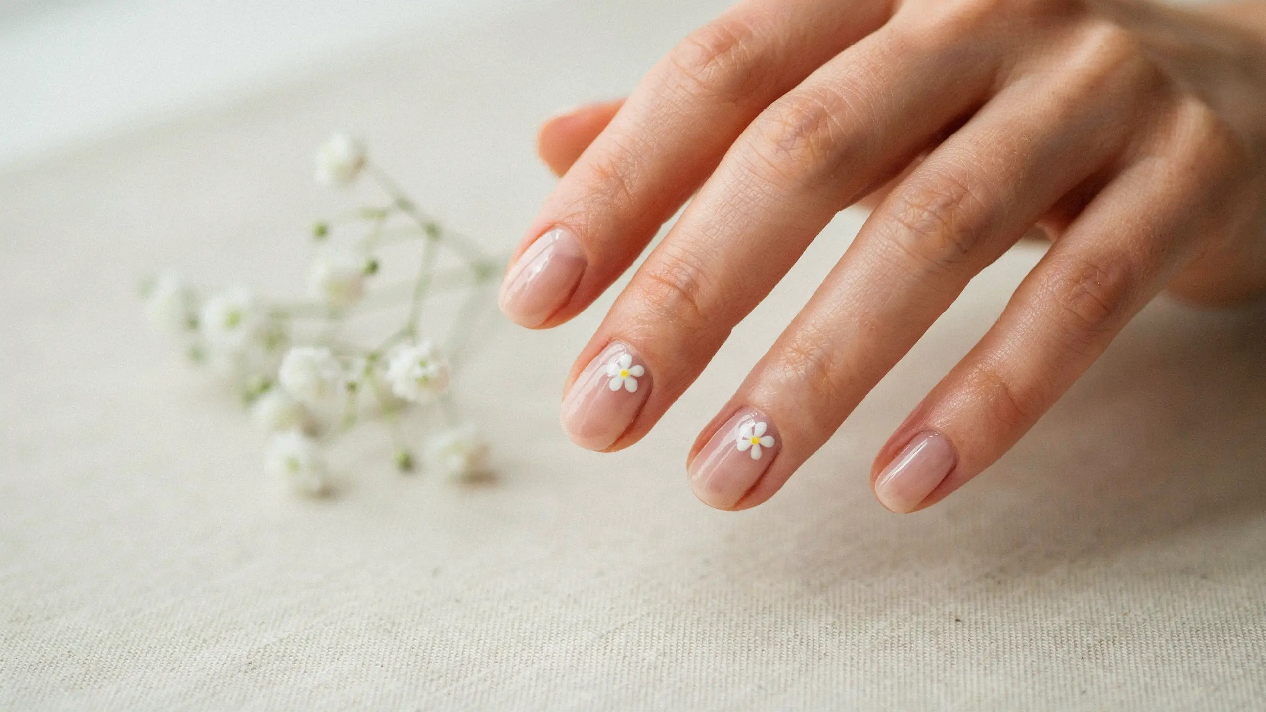 Hand with tiny flower nail art featuring small white floral details on glossy natural pink nails