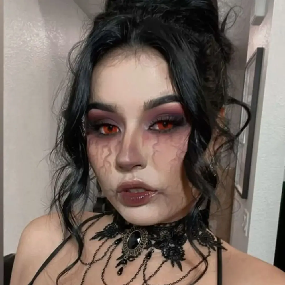 Vampire vixen makeup with ashen matte skin, smoky eyes, deep red stained lips, and small bloody neck puncture marks