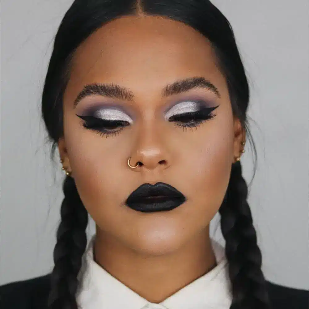 Wednesday Addams makeup with ashen matte skin, straight dark brows, subtle crisp black liner, and a muted mauve lip