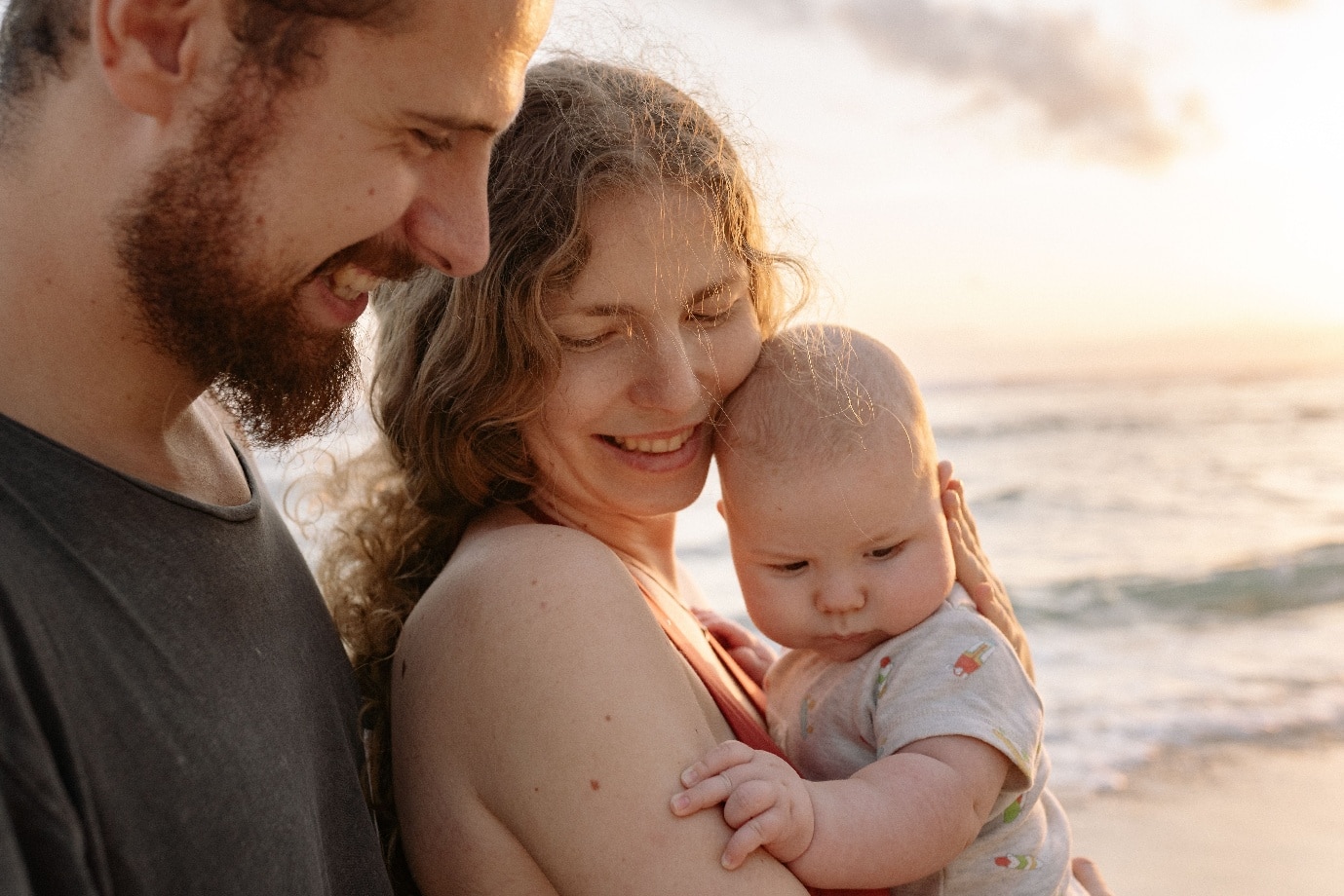 Family cuddling on the beach at sunset with ocean in background