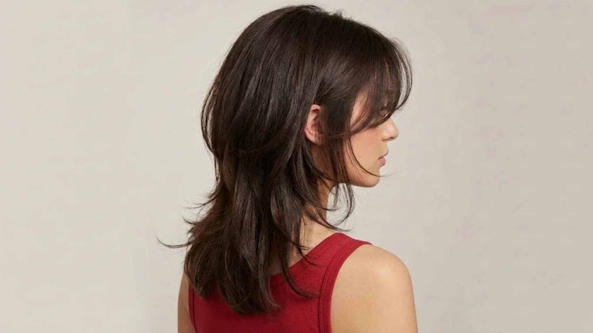 Woman showcasing a butterfly haircut with soft blended layers, face framing pieces, and voluminous flowing hair in a studio setting