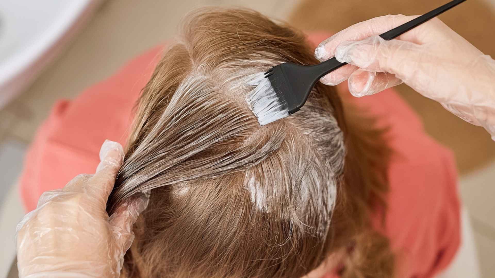 Hair dye being applied to parted hair with a tint brush during a coloring treatment.