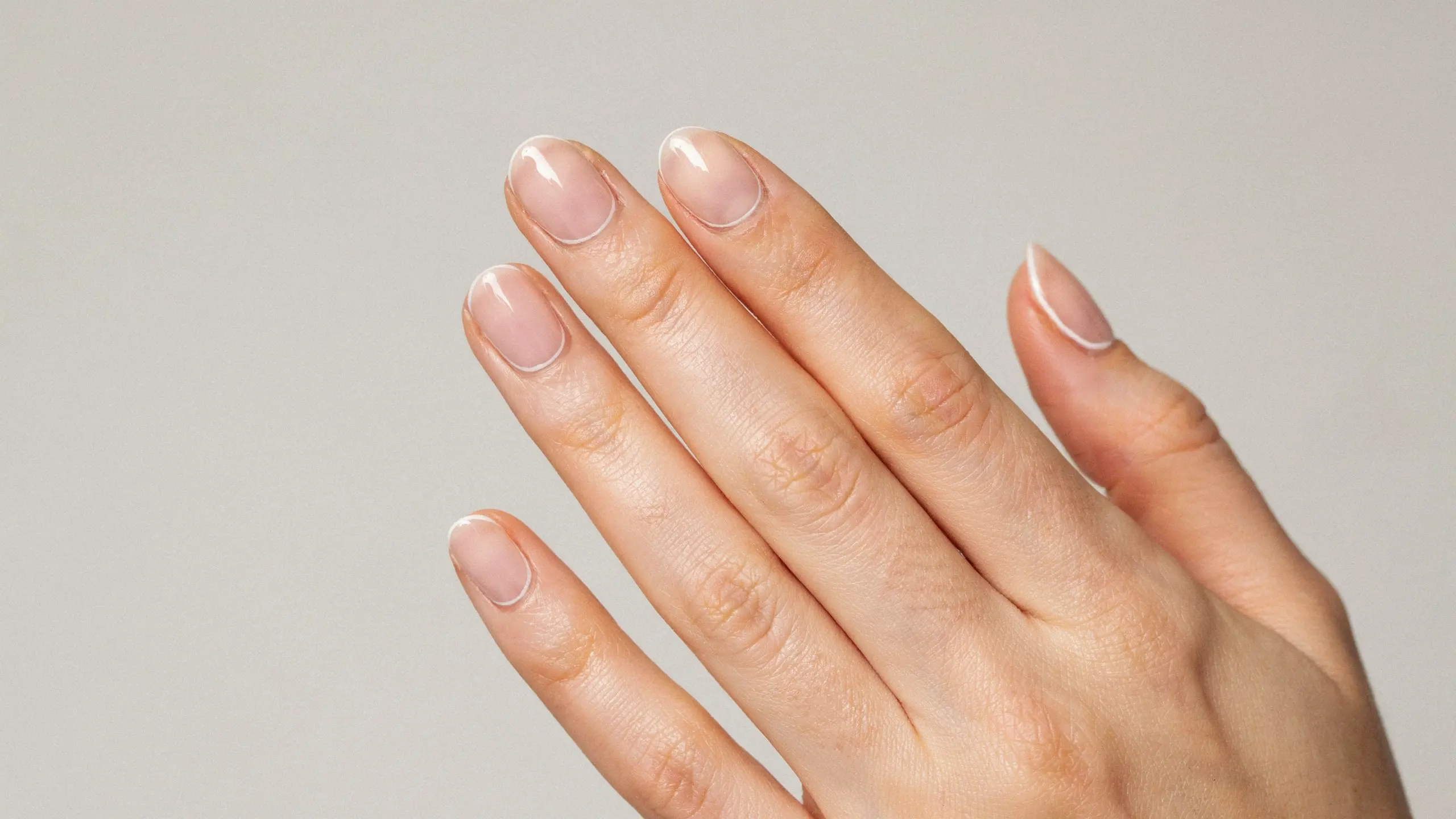 Hand with white outline nails featuring thin curved borders on glossy nude polish against a simple background
