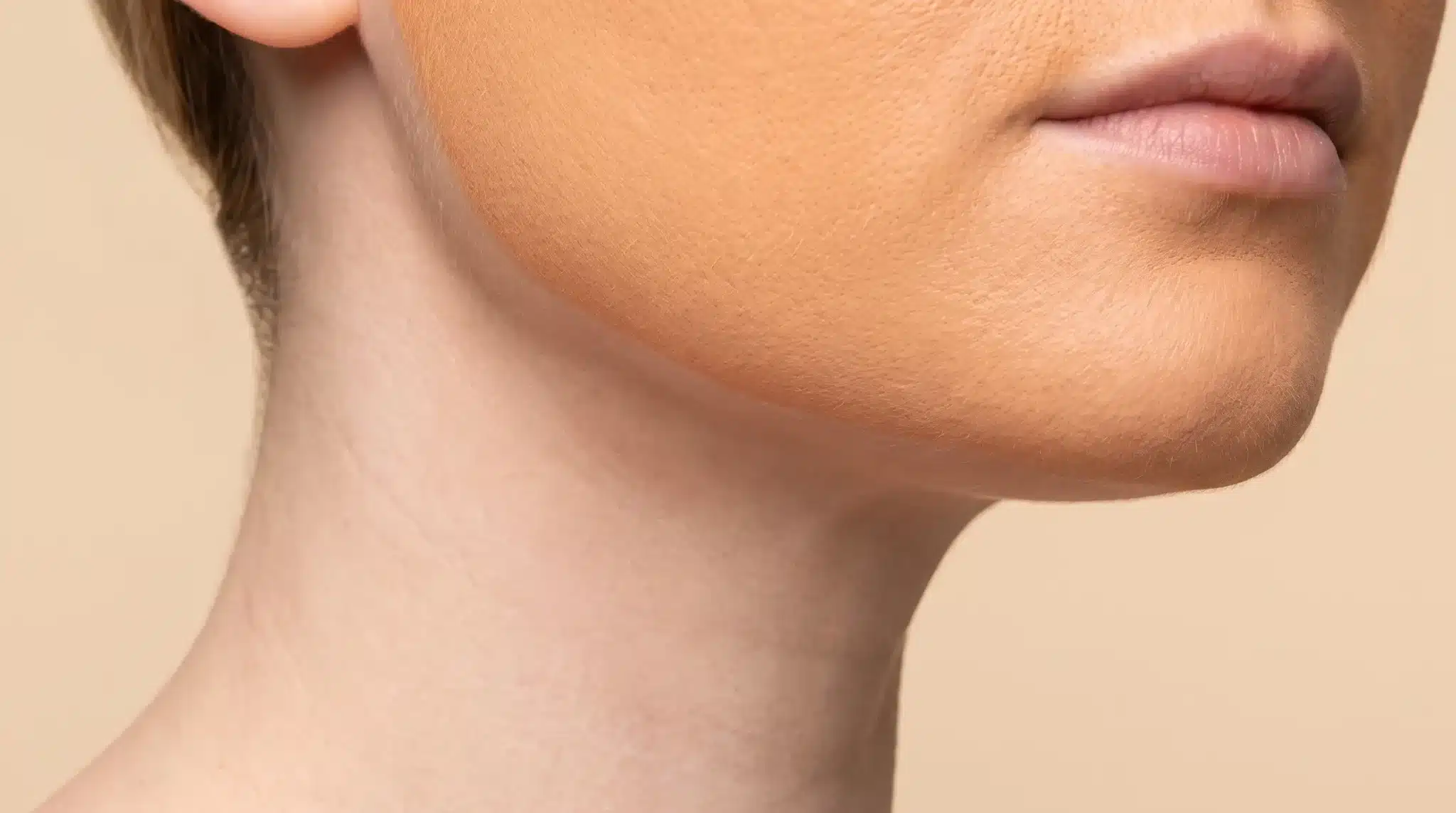 Close-up of a person's chin and jawline with visible makeup in natural lighting