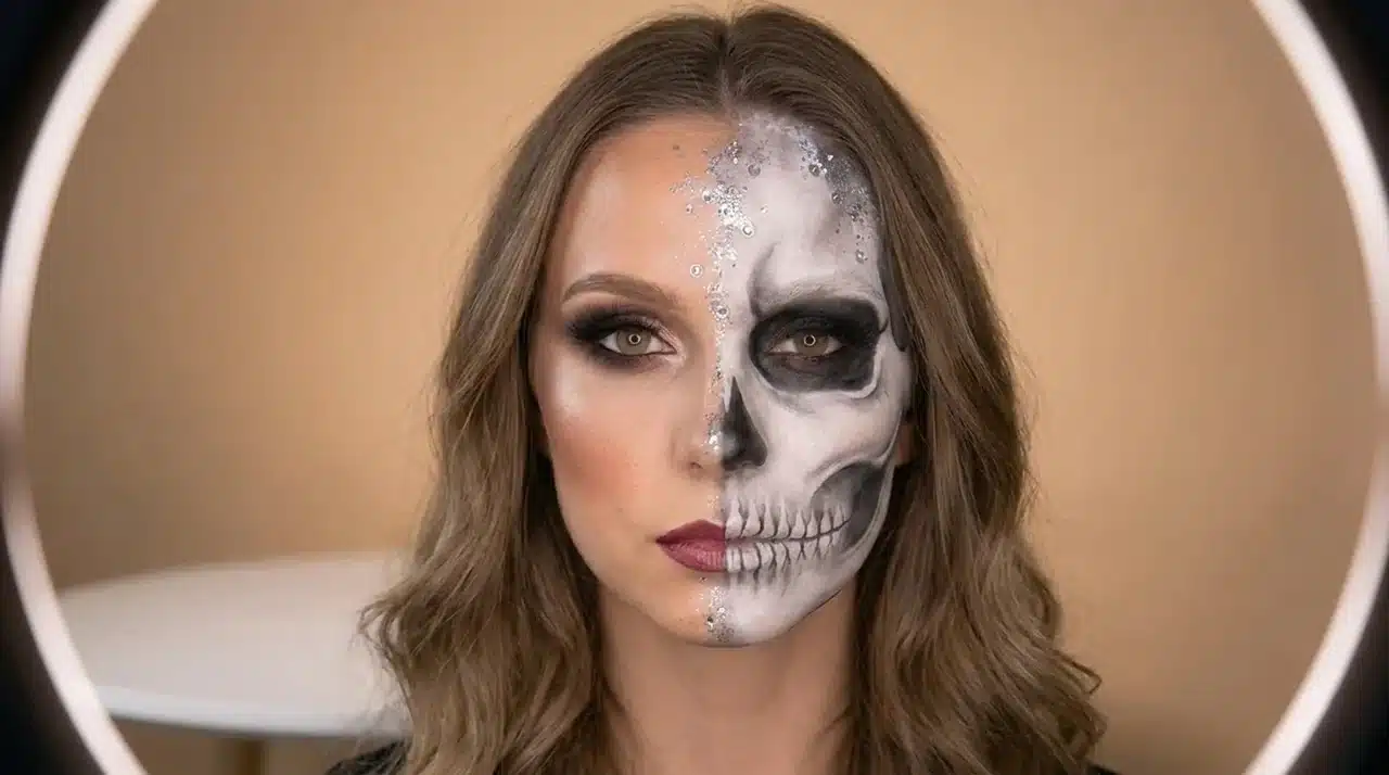 Pretty half skull makeup look featuring glamorous beauty makeup on one side and detailed skull face paint with bone shading on the other side.