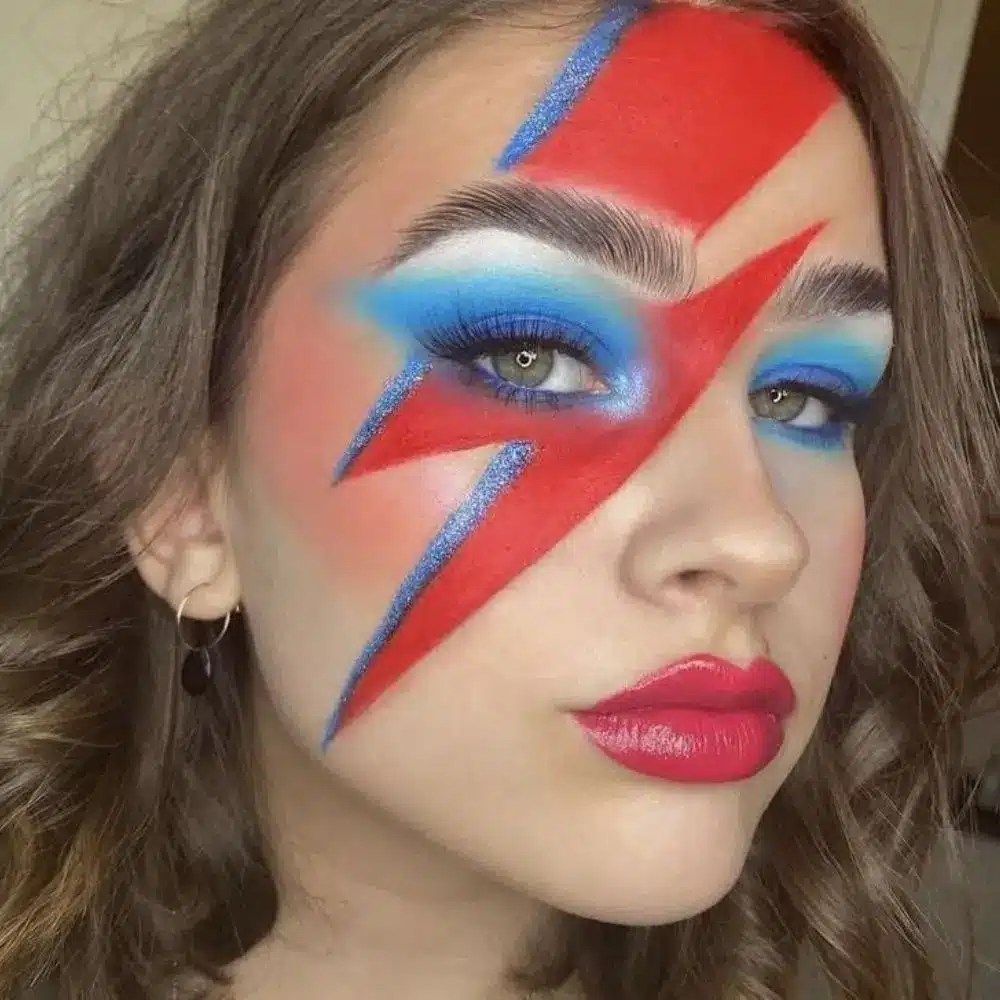 Ziggy Stardust makeup with pale matte skin, metallic eye color, black liner and a red lightning bolt across one eye